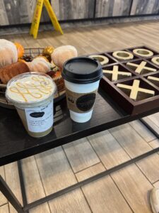 Two cups of coffee on a table with a tic tac toe board and fall decor in the background