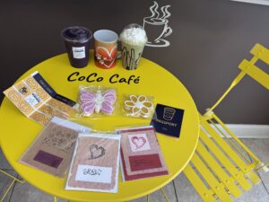 Drinks, cards, a mug and a coffee passport sit on a yellow table that says "CoCo Cafe"