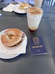 A breakfast sandwich and cup of iced coffee with coffee crawl passport on a table