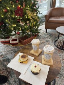 two coffees and a breakfast sandwich and pastry on a table with a holiday tree in the background